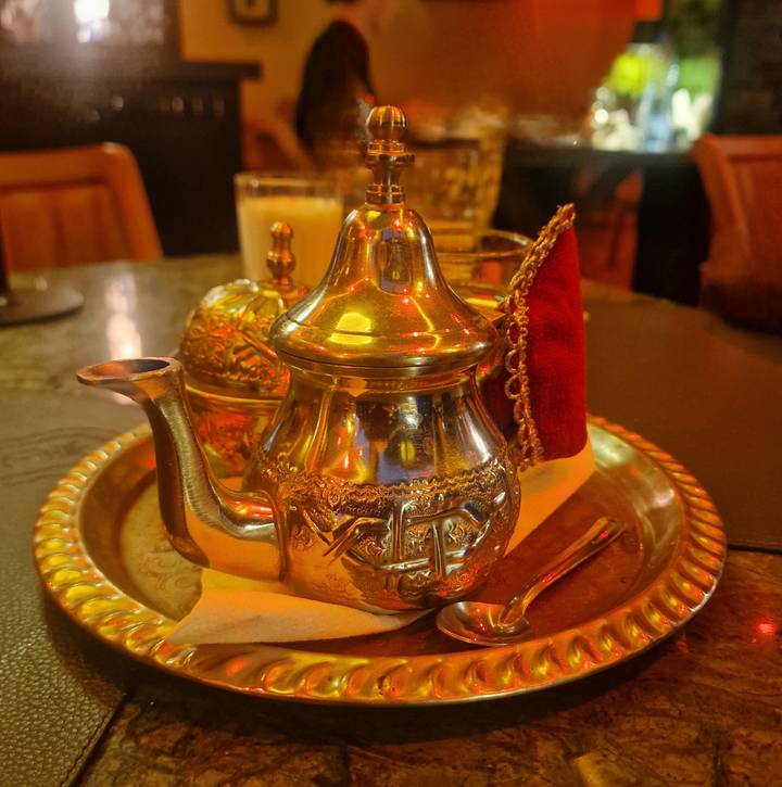 Traditional Moroccan silver teapot and cups on ornate brass tray under warm ambient lighting