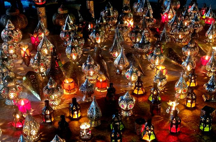 Assortment of intricate metal lanterns glowing in vibrant colors at a Moroccan market stall