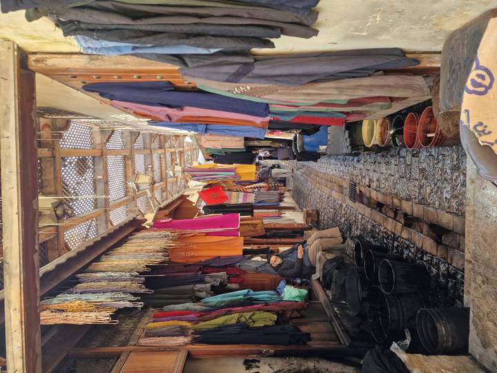 Narrow covered alley of a traditional Fes dye market with colourful hanging textiles and workers