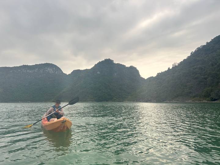 Person paddling a yellow kayak on emerald waters surrounded by towering limestone islands under soft light