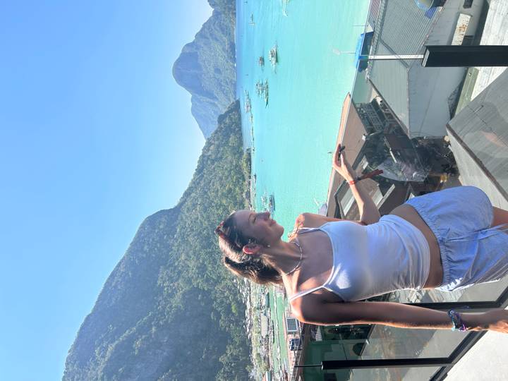 Smiling traveller on balcony overlooking vivid blue bay and surrounding green mountains