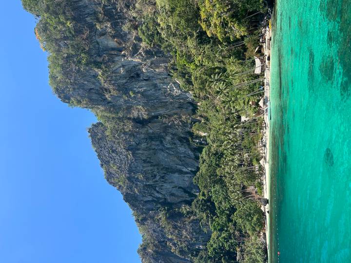 Steep limestone cliff and lush shoreline rising above crystal-clear turquoise water