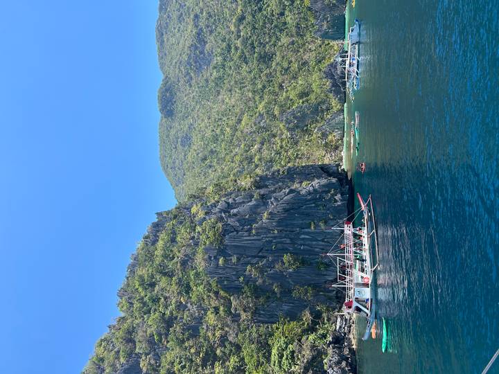 Traditional outrigger boats anchored below dramatic karst cliffs on deep blue sea