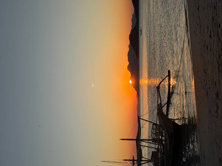 Serene sunset over calm sea with silhouette of wooden boat and golden reflection