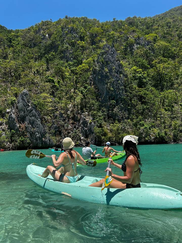 Kayakers paddle through emerald water surrounded by steep limestone cliffs covered in dense greenery.
