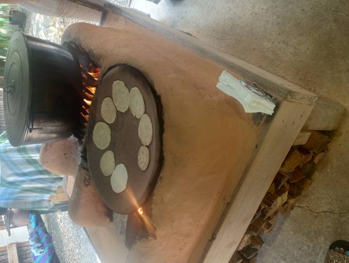Traditional clay stove with open flame cooking small tortillas on a comal