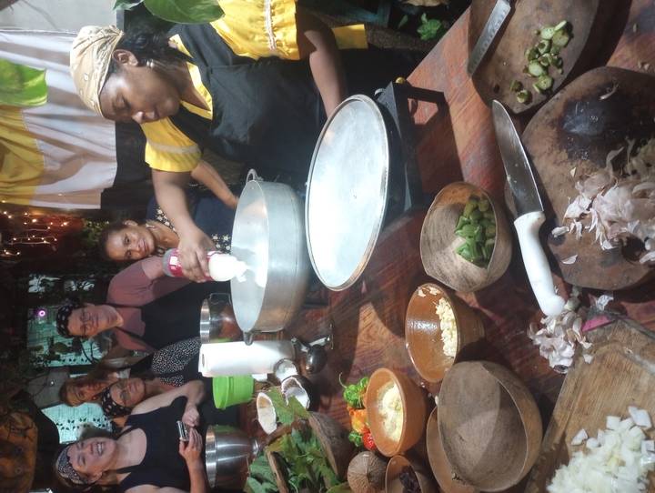Cooking demonstration with local chef pouring coconut milk while tourists watch around a rustic table