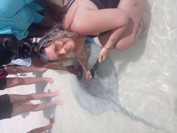 Tourist smiling while gently touching a stingray in shallow turquoise water