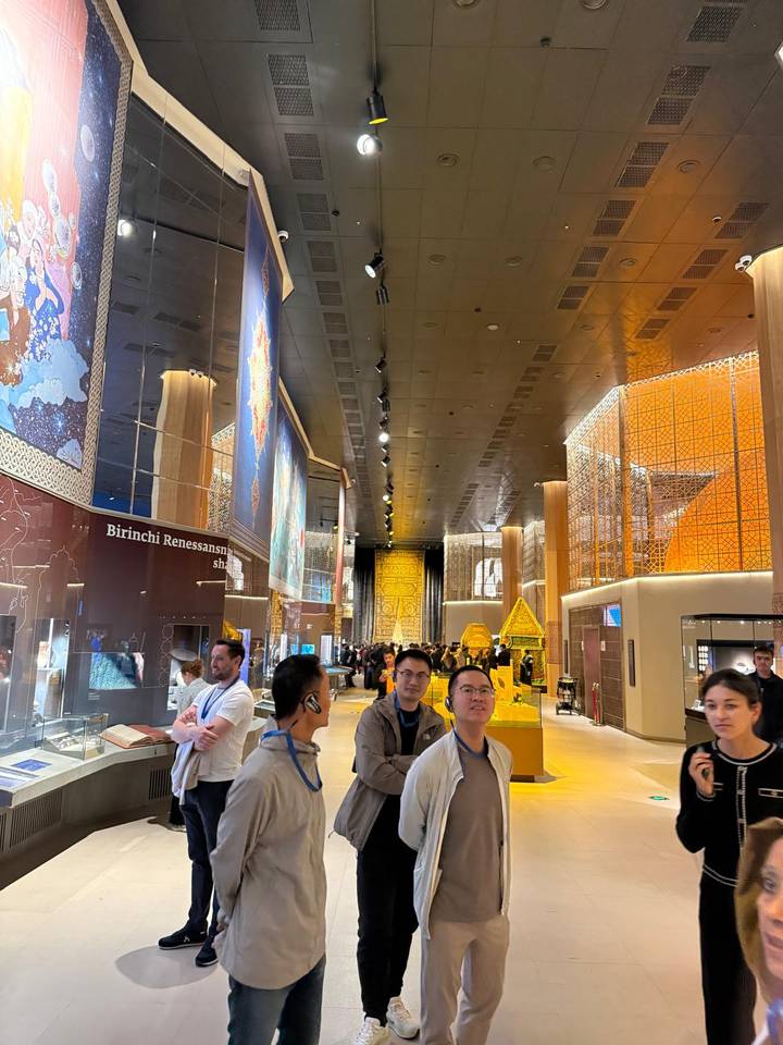 Visitors explore a modern, brightly lit museum hall with ornate decorative panels and exhibits.