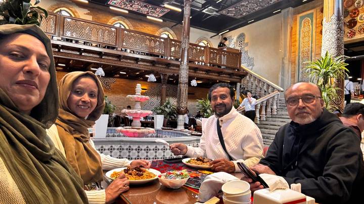 Four diners smile around a table laden with Uzbek dishes in a richly decorated restaurant interior.