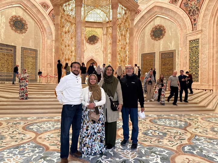 A small group poses on ornate marble steps beneath a grand golden interior dome with Islamic motifs.