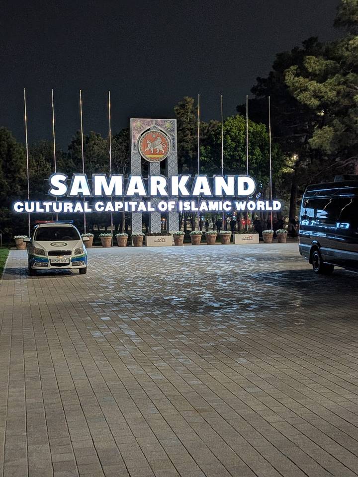 Night view of an illuminated city sign reading 'SAMARKAND Cultural Capital of Islamic World'.