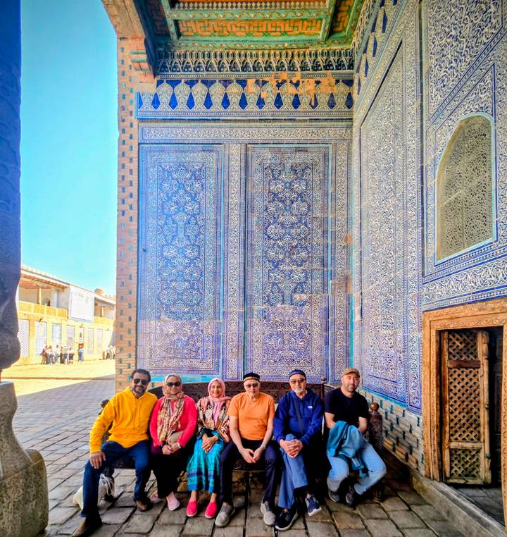 Group portrait against vivid blue patterned tiles inside a historic site, slightly overexposed.