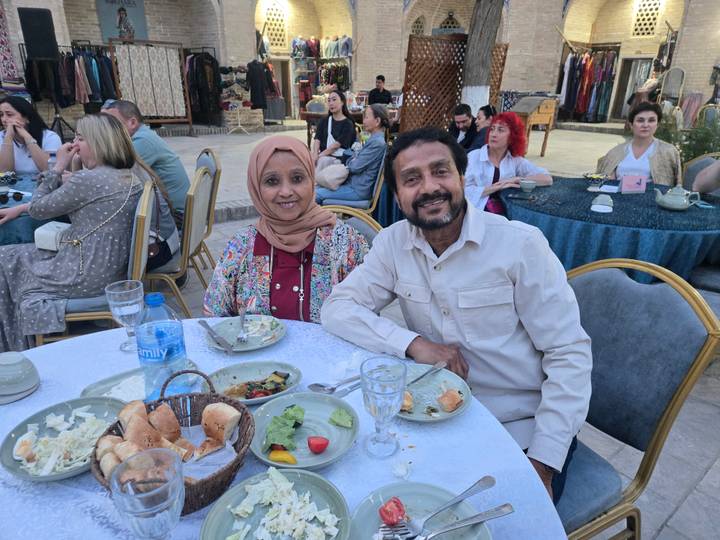 Smiling couple seated at an outdoor banquet table with partly eaten dinner plates during an evening event.