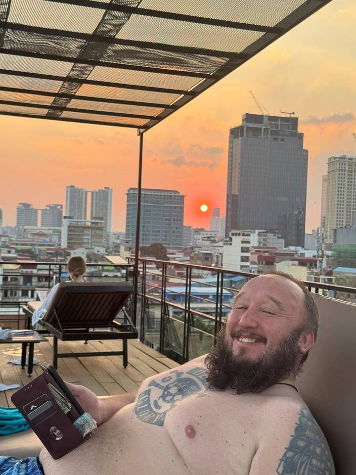 Sunset view over a modern city skyline from a rooftop terrace where travellers relax by loungers.