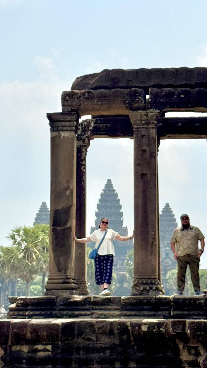 Travellers pose between stone pillars framing the iconic spires of Angkor Wat in the distance.