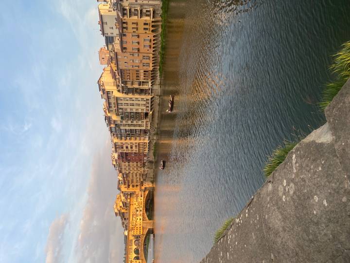 Golden light falls on riverside buildings along the Arno with small boats on the calm water
