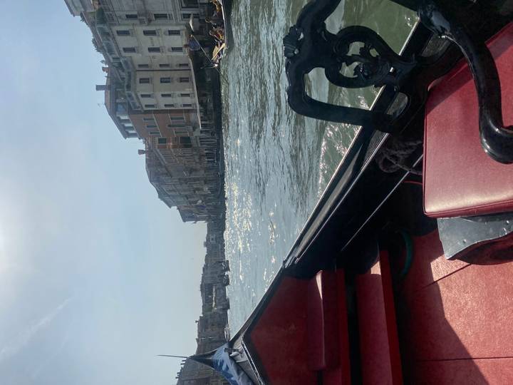 View from inside a gondola gliding along a shimmering Venetian canal beneath sunny skies