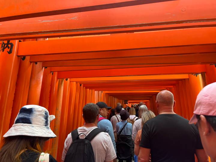Crowd walking under the endless bright orange torii gates of Fushimi Inari shrine passageway.