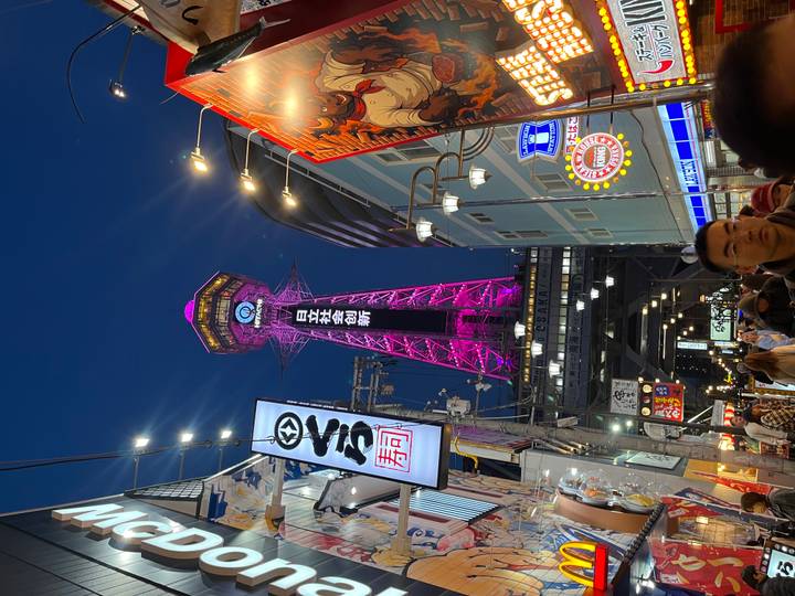 Night scene in Osaka’s Shinsekai district with the Tsutenkaku Tower glowing bright pink above lively food stalls.