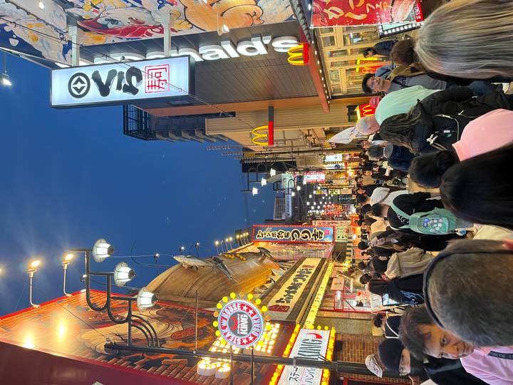Busy pedestrian street in Osaka at dusk lined with bright restaurant signs and fast-food icons.
