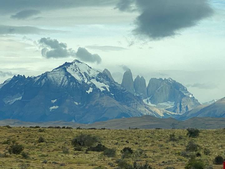 Wide view of the jagged Torres del Paine massif dusted with snow under a moody sky above Patagonian steppe.