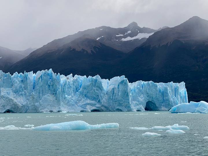 Jagged ice spires of Perito Moreno Glacier towering over a milky-green lake with misty mountains beyond.