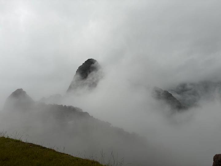 Heavy fog obscures the iconic peak of Huayna Picchu and surrounding mountains, with ruins barely visible.