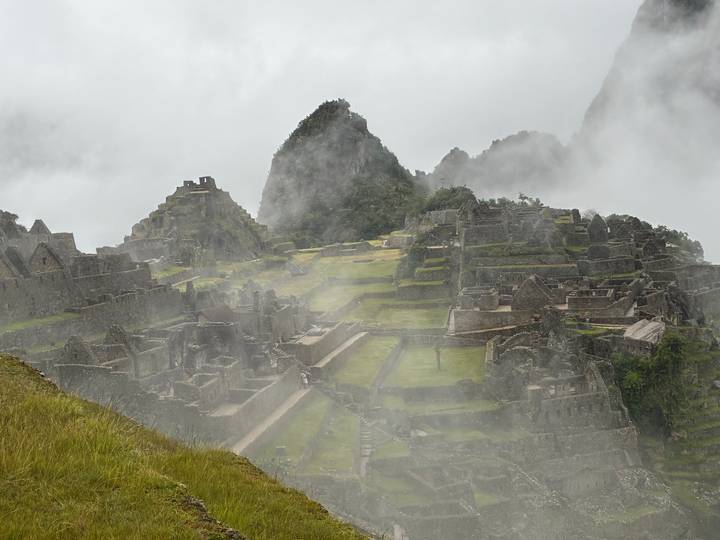 Partially mist-covered terraces and stone structures of Machu Picchu with lush green backdrop.
