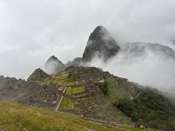 Stone ruins and terraces of Machu Picchu framed by swirling clouds with iconic peaks behind.