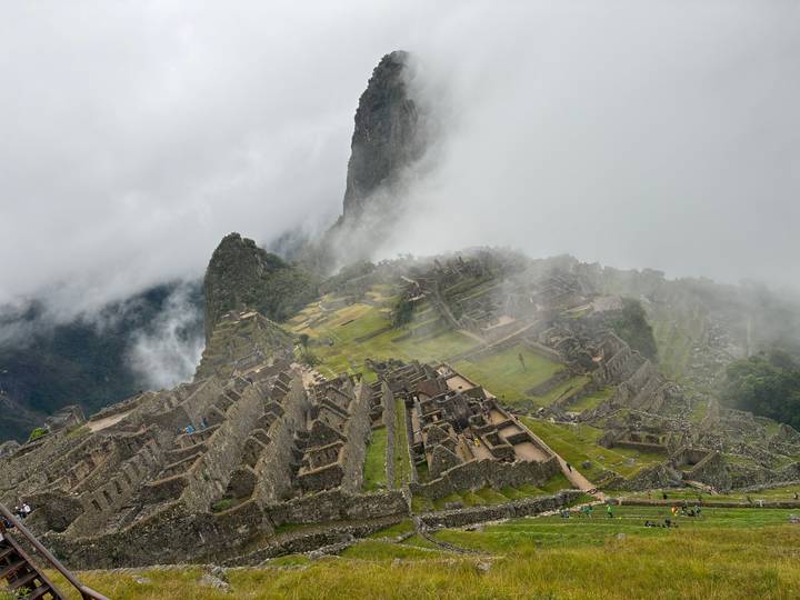 Angled bird’s-eye view of Machu Picchu ruins with drifting mist revealing intricate stonework.