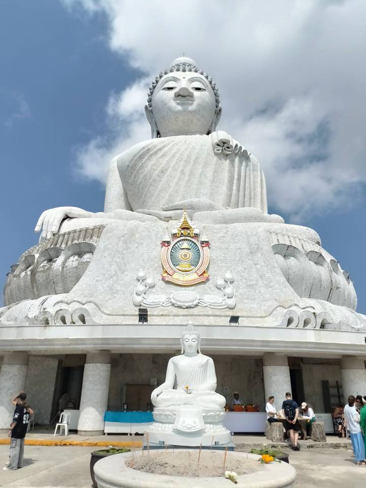 Close detail of the colossal white Buddha statue against blue sky with royal emblem on chest.
