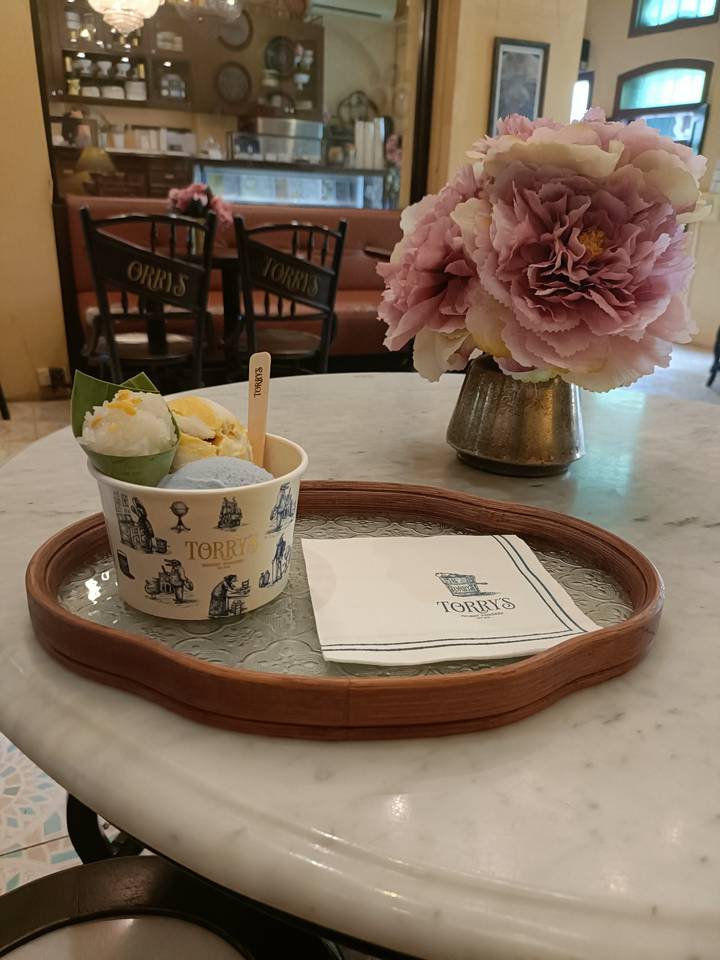 A cup of artisan ice cream on a wooden tray in a stylish café, with flowers and branded napkin.