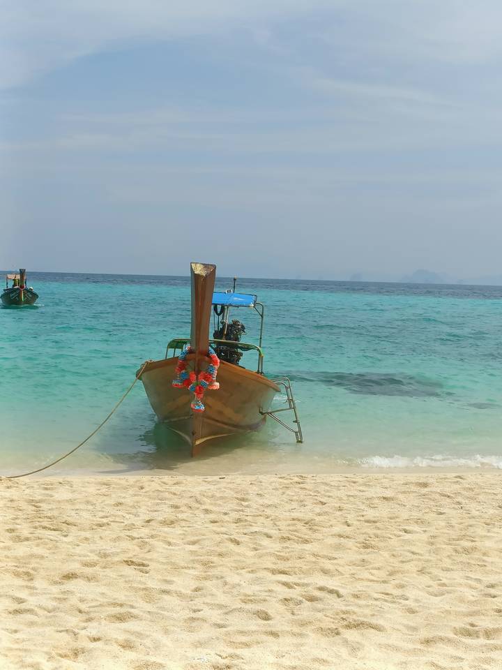 A decorated Thai long-tail boat is moored in crystal-clear turquoise water off a white sand beach.