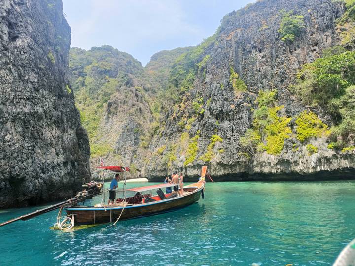 A long-tail boat glides through turquoise water between towering limestone cliffs covered in greenery.