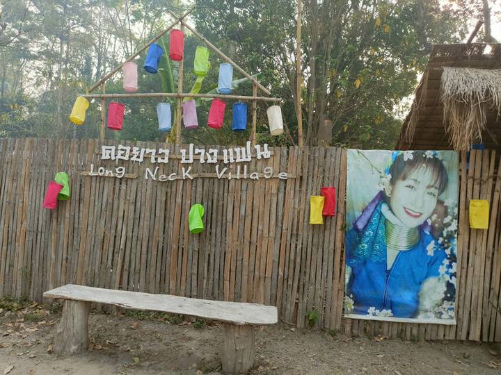 Entrance sign reading 'Long Neck Village' on a bamboo fence decorated with colorful lanterns.