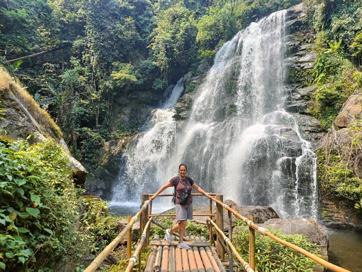 Woman stands on a wooden viewing platform before a powerful jungle waterfall cascading over rocks.