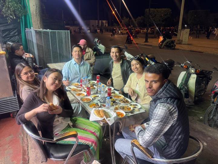 Friends gathered around a table filled with Moroccan dishes at a lively night-time street eatery