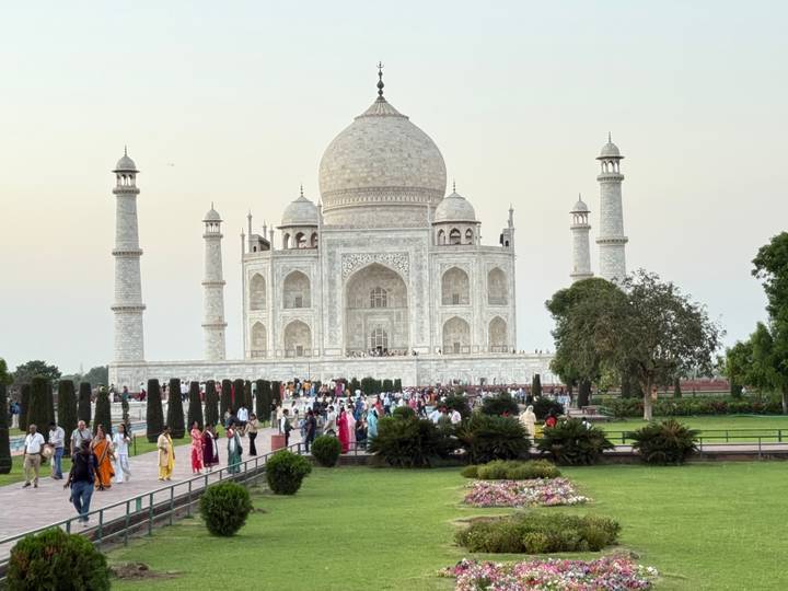 The Taj Mahal at dusk with crowds of visitors walking along the marble pathway.