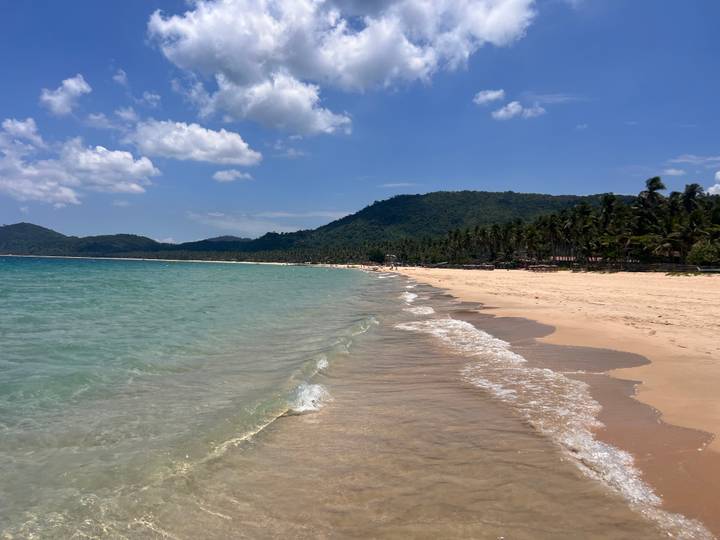 Pristine sandy beach with turquoise water and palm-lined hills under a clear sky.