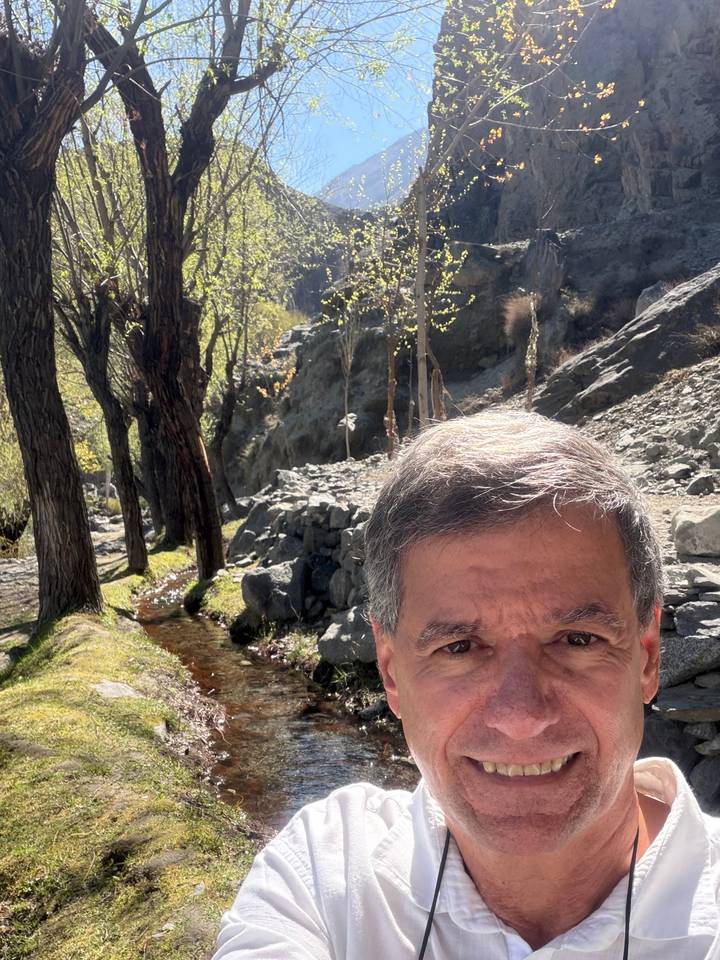 Partial selfie of man with rocky woodland stream and sunlit cliff behind