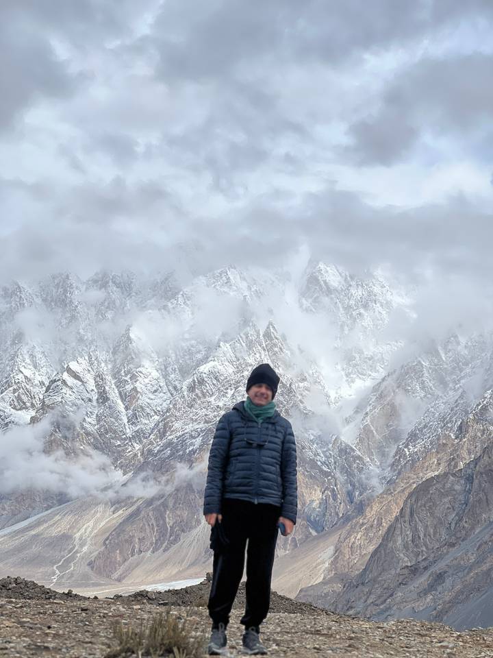 Man in front of mist-covered jagged snowy mountains partially hidden by clouds