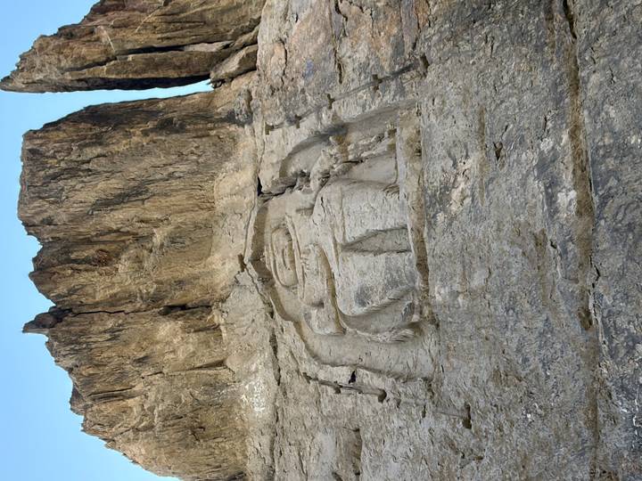 Ancient Buddha bas-relief carved high on rock cliff