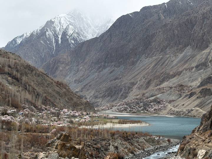Wide valley view of turquoise lake, blossoming villages and snow-capped peaks