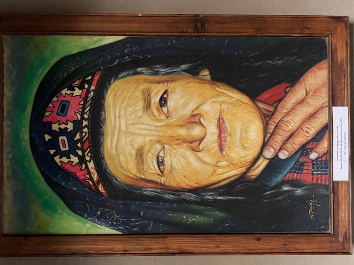 Photograph of a detailed painting portraying an elderly woman in traditional attire displayed on a wall.