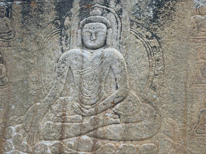 Ancient rock relief of a seated Buddha figure carved into weathered stone.