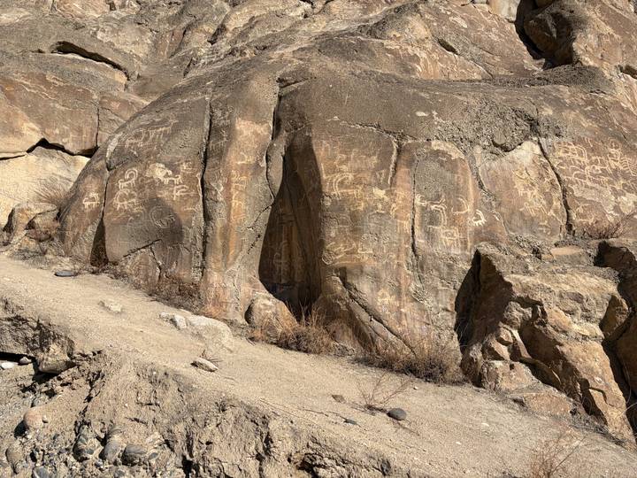 Sun-lit cliff face covered with ancient petroglyphs etched into the weathered brown rock.