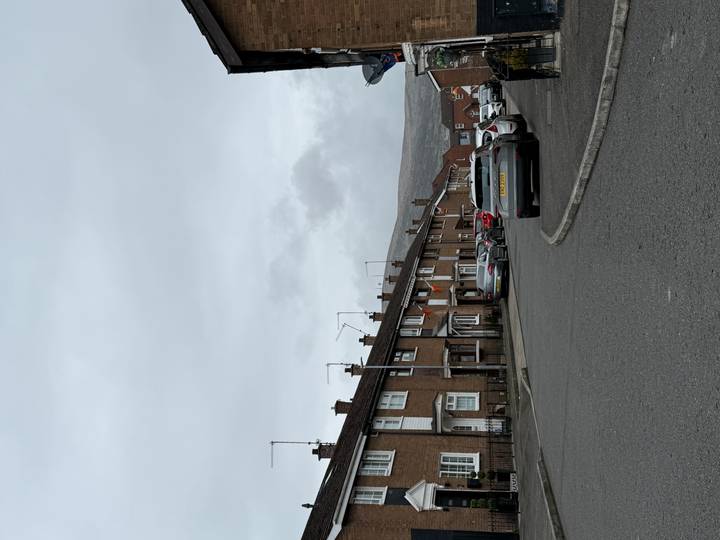 Quiet row of brick terraced houses on a grey overcast morning with hills faintly visible behind.