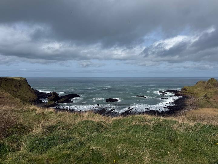 Grassy headlands frame a moody seascape of choppy grey waves under heavy cloud cover.