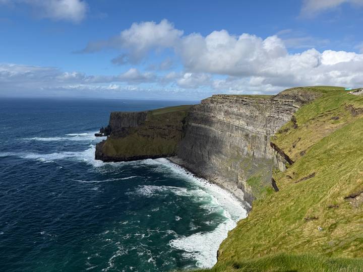 Sheer Atlantic cliffs dropping into deep blue sea with white surf below and grassy headland above.